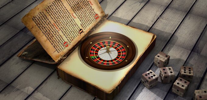 Na tle drewnianej podłogi ruletka w środku otwartej księgi, obok 6 rozrzuconych kości do gry.