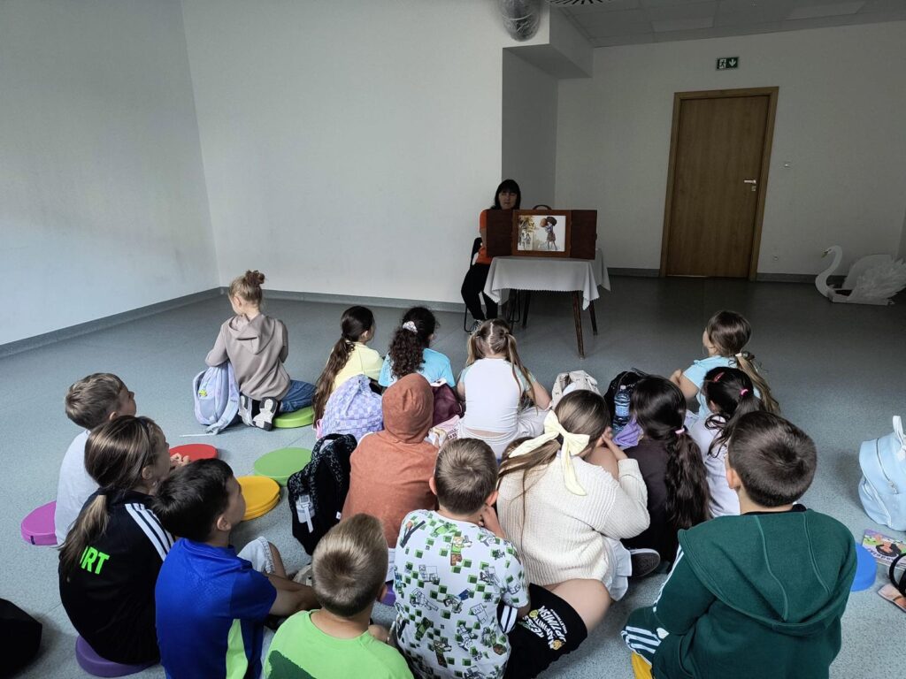 Nauczyciel czytający opowiadanie za pomocą teatrzyku kamishibai, dzieci siedzą przed.