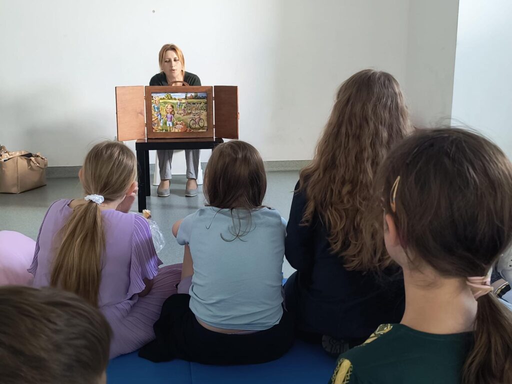 Nauczyciel czytający opowiadanie za pomocą teatrzyku kamishibai, dzieci siedzą przed.